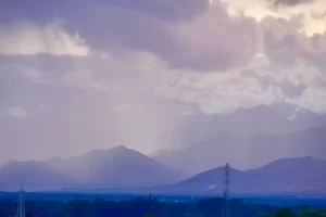 Dramatic mountain scene with cloud cover, light rainfall, and power lines, offering serene beauty