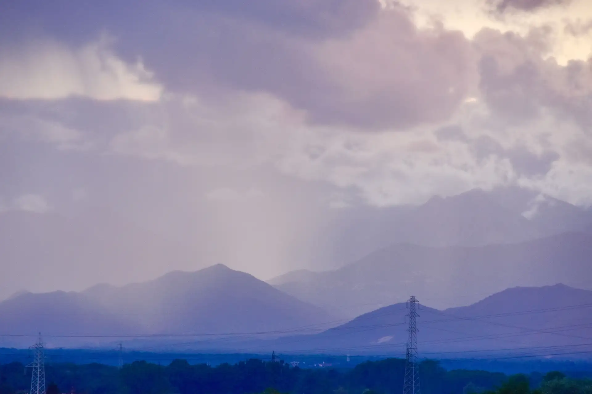 Dramatic mountain scene with cloud cover, light rainfall, and power lines, offering serene beauty