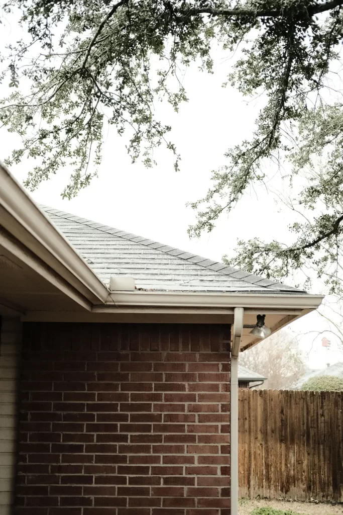 A serene view of a red brick house corner with cleaned gutters and overhanging tree branches