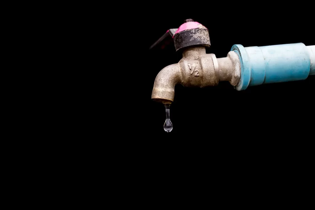A detailed view of a metal faucet with a single water drop against a black background